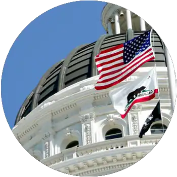 The American flag and State of California flag are raised in front of the Sacramento State Capitol.