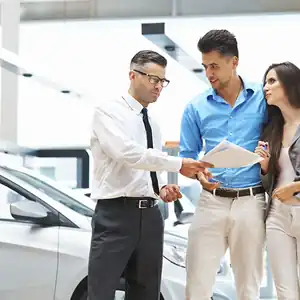 Photo of a car salesman handing paperwork to a couple buying a car
