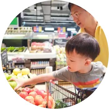 An Asian man is in a grocery store with his young son who sits in a shopping cart.