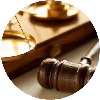 A wooden judge’s gavel lies on a desk next to a set of copper scales.