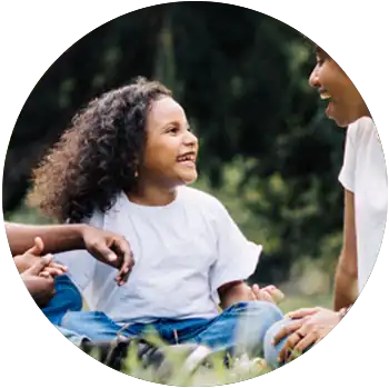 A young Black girl with curly hair smiles at her mom and holds hands with her father in a field.